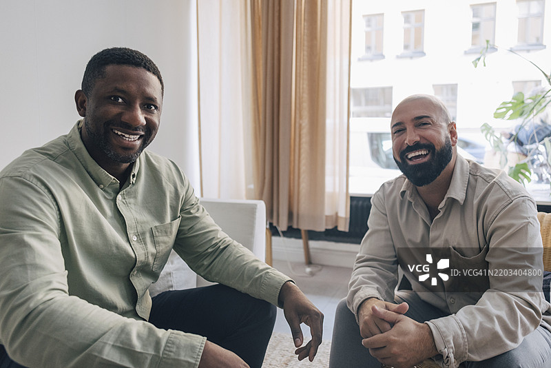 快乐的男性商务专业人士在办公室享受休息时间，彼此交流。图片素材