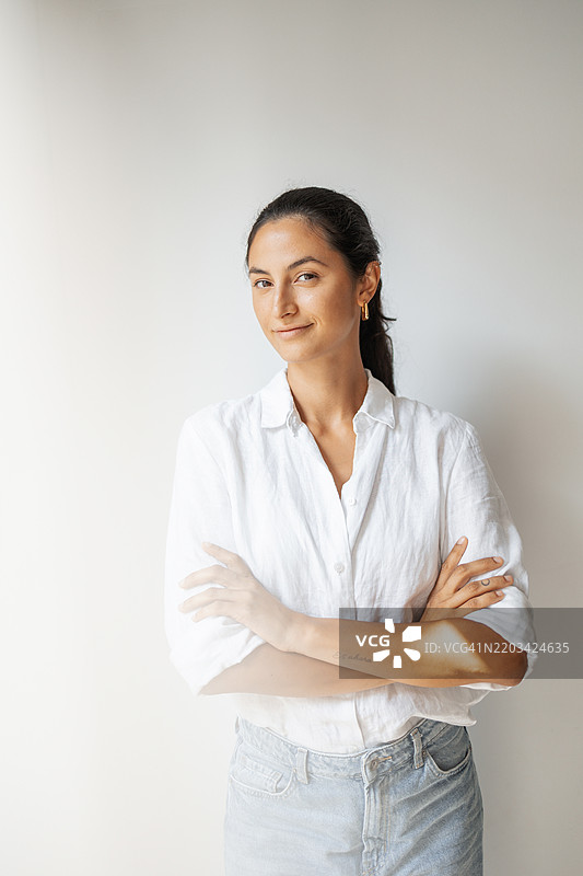 自信的女性穿着白衬衫在中性色背景前微笑图片素材