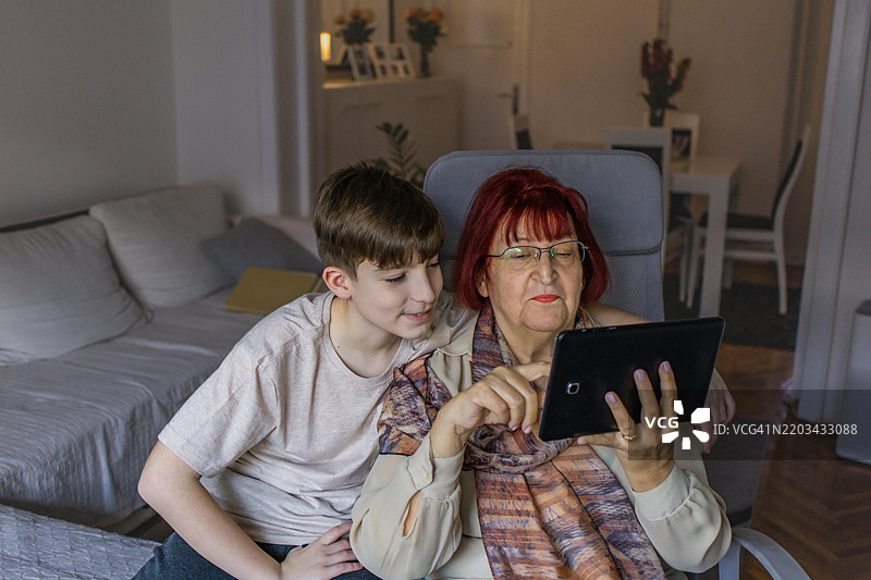 多代同堂的家庭享受亲密时刻。祖母和她的孙子在家中使用平板电脑学习新知识。图片素材
