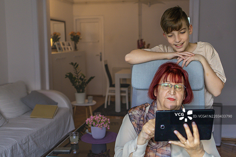 多代同堂的家庭享受亲密时光。祖母和她的孙子在家中使用平板电脑学习新知识。图片素材