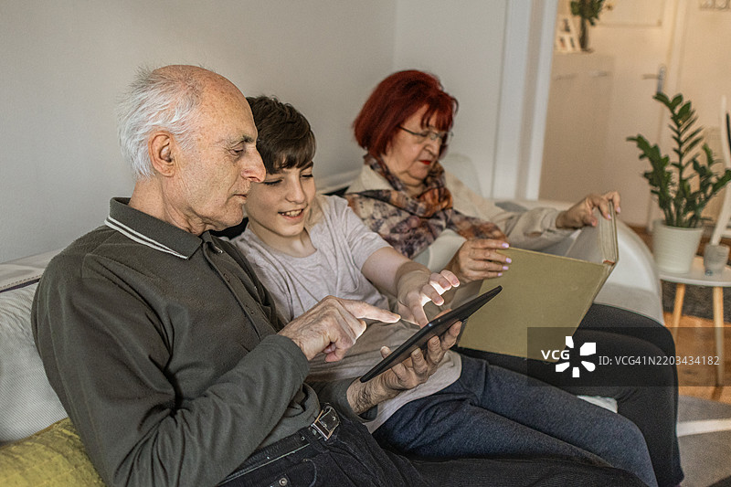 多代同堂的家庭享受亲密时光。祖父母和他们的孙子在家中使用数字平板学习新知识。图片素材