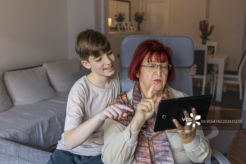 多代同堂的家庭享受亲密时光。祖母和她的孙子在家中使用平板电脑学习新知识。图片素材