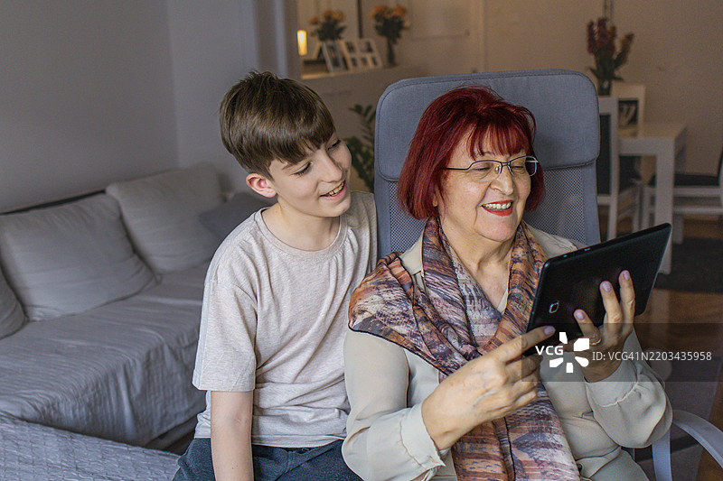 多代同堂的家庭享受亲密时光。祖母和她的孙子在家中使用平板电脑学习新知识。图片素材