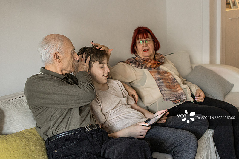 多代同堂的家庭享受亲密时刻。祖父母和他们的孙子在家中使用平板电脑学习新知识。图片素材