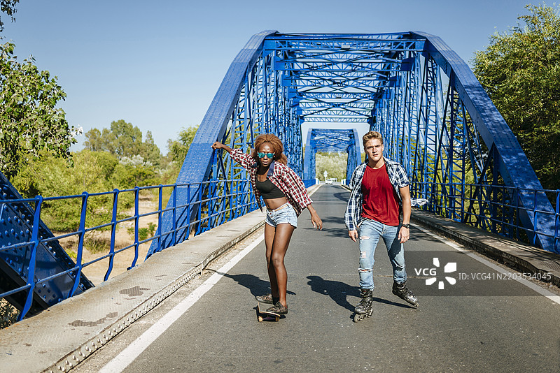 一对情侣在桥上玩滑板和直排轮滑，享受乐趣图片素材