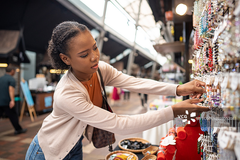 年轻女性在热闹的室内市场摊位前浏览五彩缤纷的珠宝展示图片素材