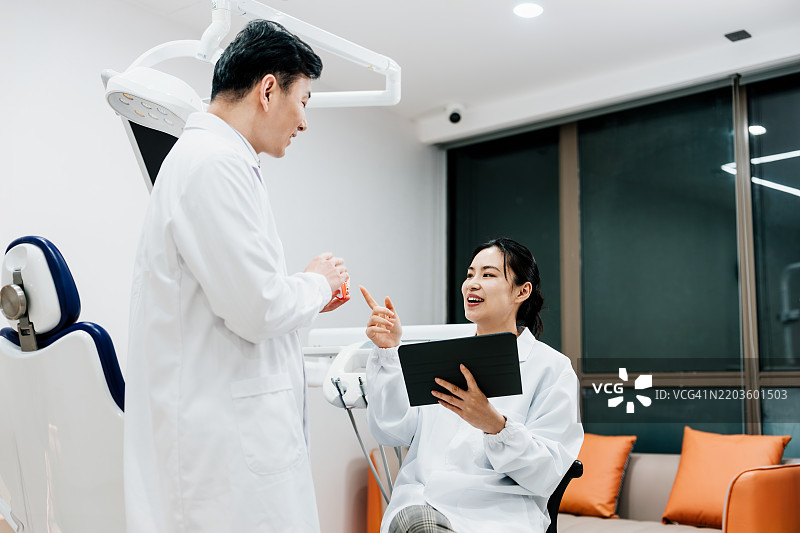 两位亚洲牙医在牙科办公室讨论数字平板上的手术计划。图片素材