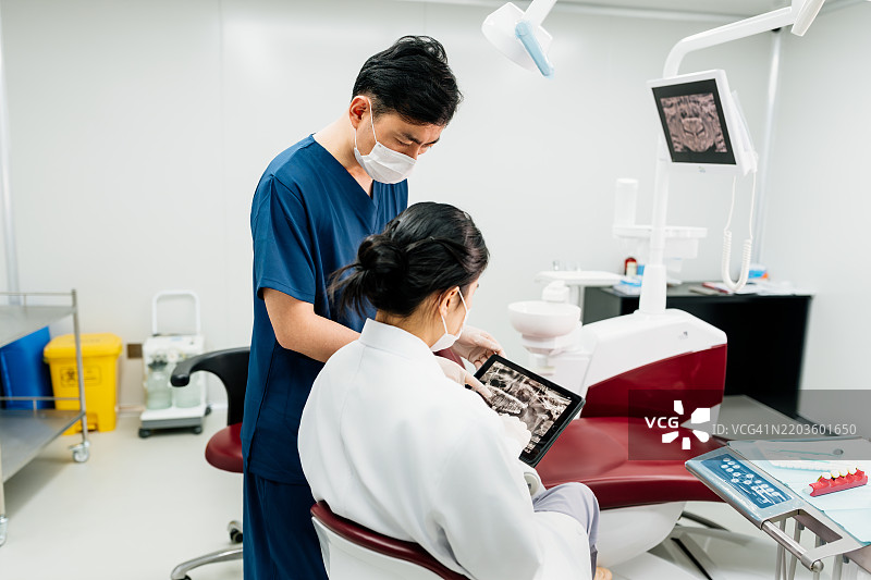 两位亚洲牙医在牙科办公室讨论数字平板上的手术计划。图片素材