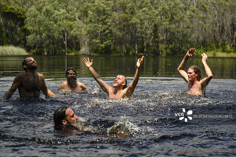 中年男子与男性朋友们在湖中微笑，双臂高举，尽情享受乐趣。图片素材