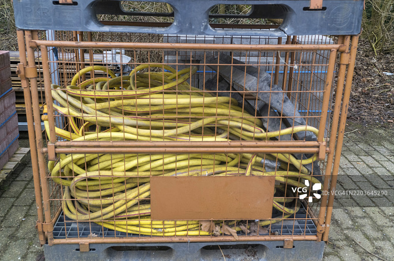 黄色工业软管整齐地放置在建筑工地的金属笼内，随时准备用于各种应用。图片素材