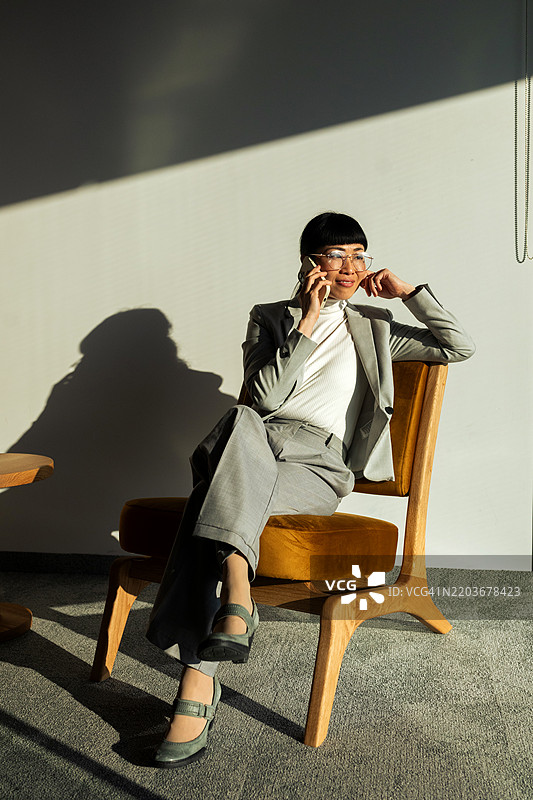 中年亚洲女商人坐在椅子上，使用智能手机进行沟通图片素材