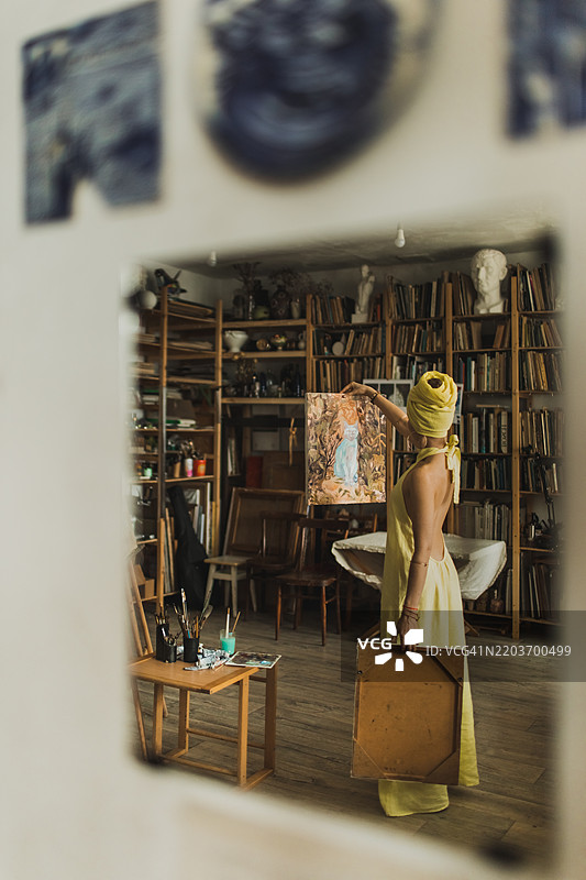 艺术工作室中，女人手持画布艺术作品的镜子反射图片素材