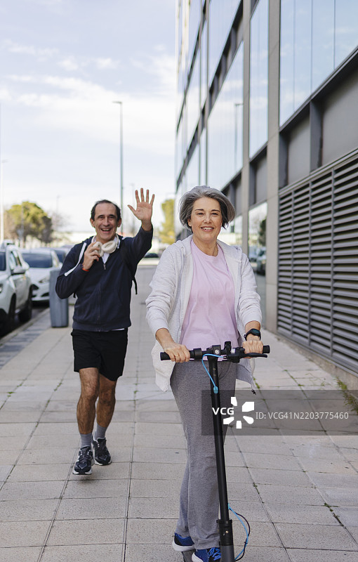 一位老年女性骑着电动滑板车，一位老年男性在后面跑着。图片素材