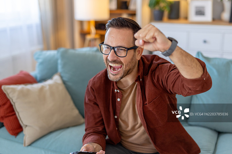 快乐的男人在沙发上与电视一起庆祝美好时刻图片素材