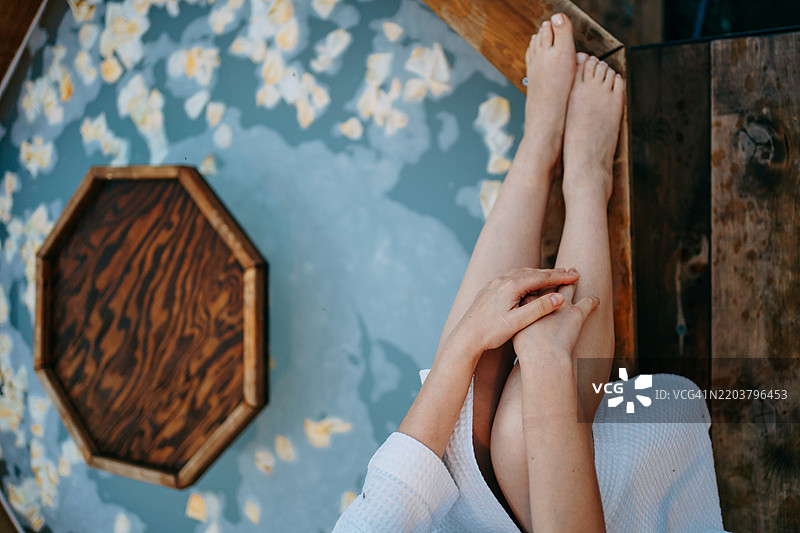 女人在木浴缸中放松，周围有花瓣和一个托盘图片素材