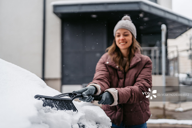 年轻女性在街上清理汽车上的雪图片素材