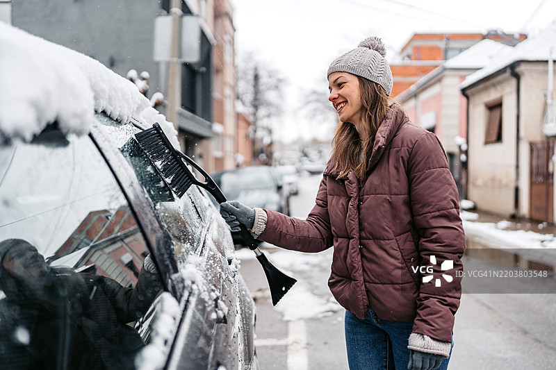 年轻女性在街上清理汽车上的雪图片素材
