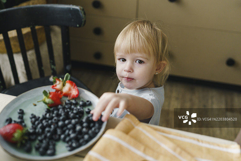 女孩在厨房的桌子上吃蓝莓图片素材