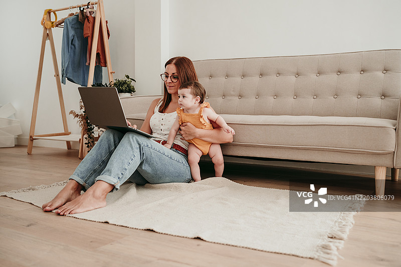女商人在家中与女儿一起坐着，使用笔记本电脑工作图片素材