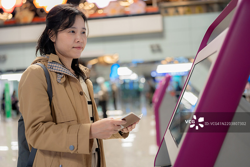 母亲和儿子在机场自助值机亭。自信的亚洲女性正在扫描护照以获取登机牌。利用现代科技、自动化和无线触摸屏服务轻松旅行，享受无压力的旅程。图片素材