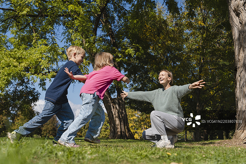 兄弟姐妹在花园里奔向蹲下双臂伸开的母亲图片素材