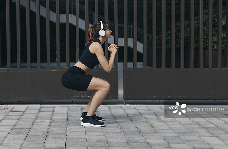 女人在人行道附近的门口戴着无线耳机锻炼图片素材
