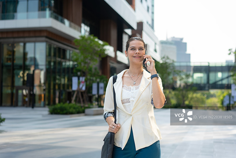 自信的女商人在城市环境中走路并打电话图片素材