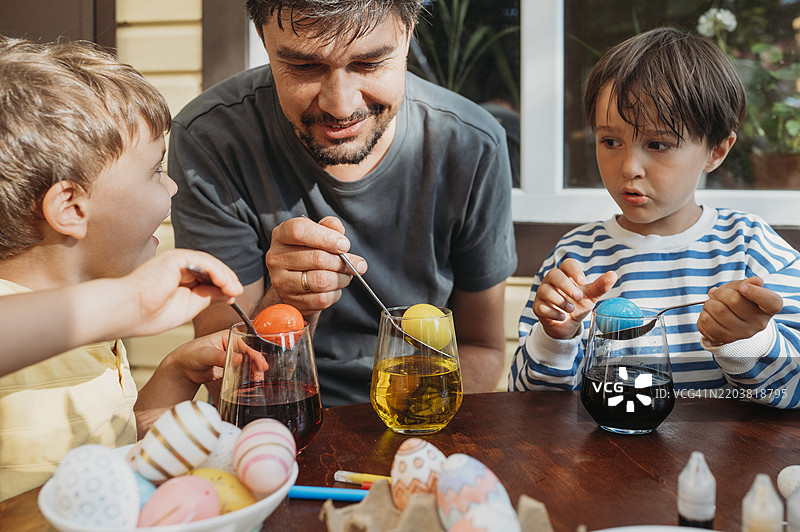 父亲和儿子们在五彩的杯子里给复活节彩蛋上色图片素材