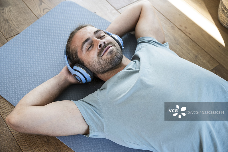 微笑的男子躺在垫子上，戴着无线耳机听音乐图片素材