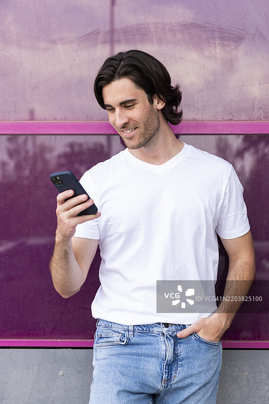 微笑的年轻男子手插口袋，使用智能手机图片素材