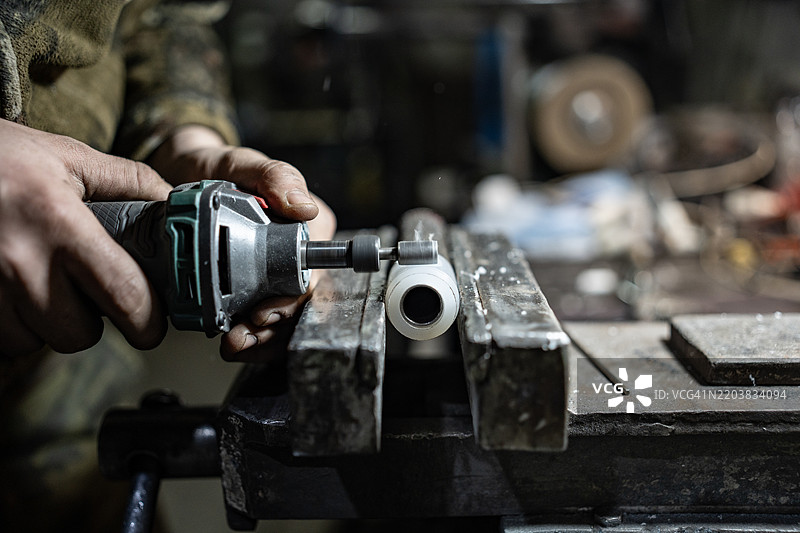 在车间使用电动工具和金属管进行手动打磨过程图片素材
