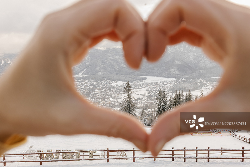 冬季山脉前，一位女性的手势形成心形。图片素材