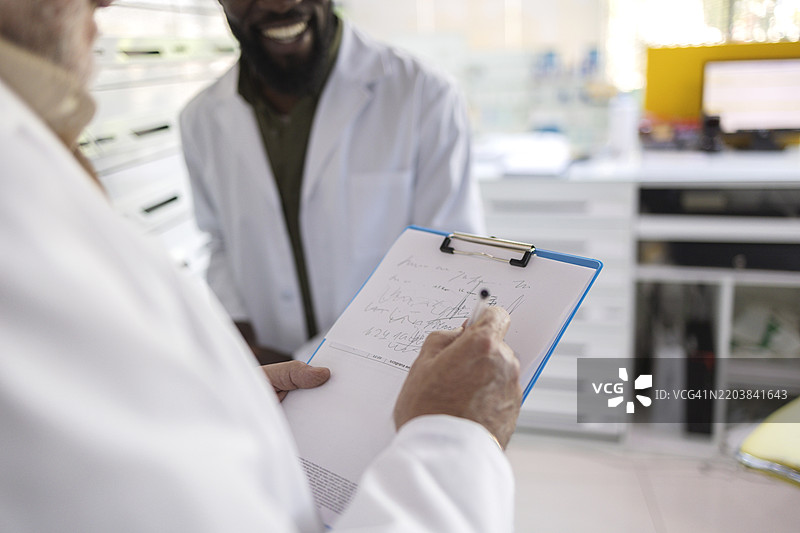 快乐的药剂师与同事在药房用夹板写药方图片素材