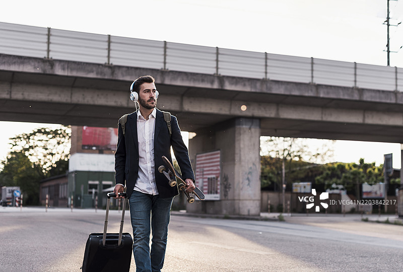 年轻商人手提行李箱，骑着滑板在路上行走图片素材