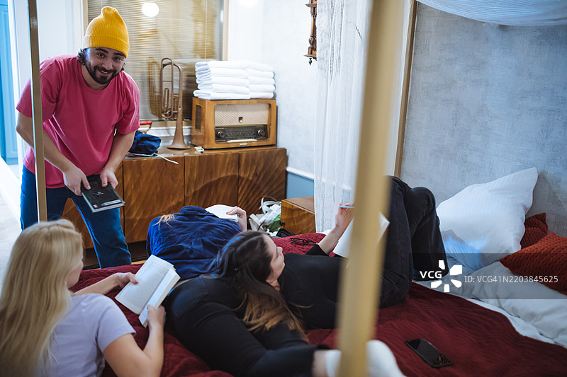 有趣的学习时光被打断：朋友们在床上学习，一名男子跳了进来！幽默且贴近年轻文化与学生生活的照片。图片素材