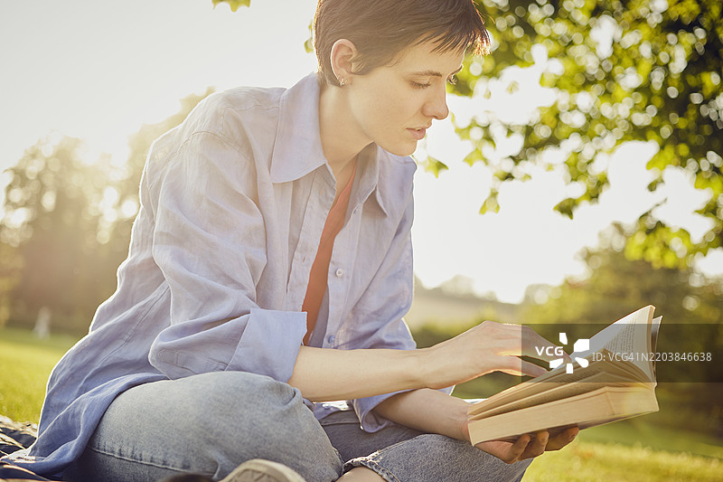 年轻女性在公园里盘腿坐着阅读书籍图片素材