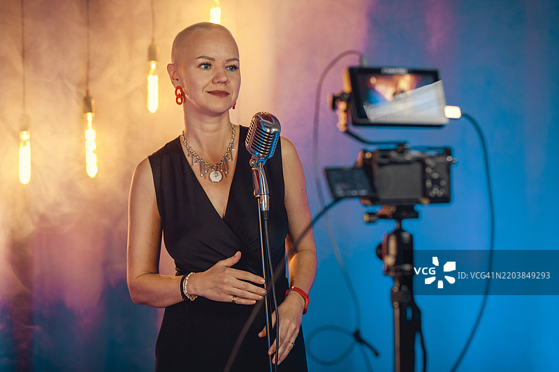 微笑的歌手在录音室用麦克风通过摄像机拍摄图片素材
