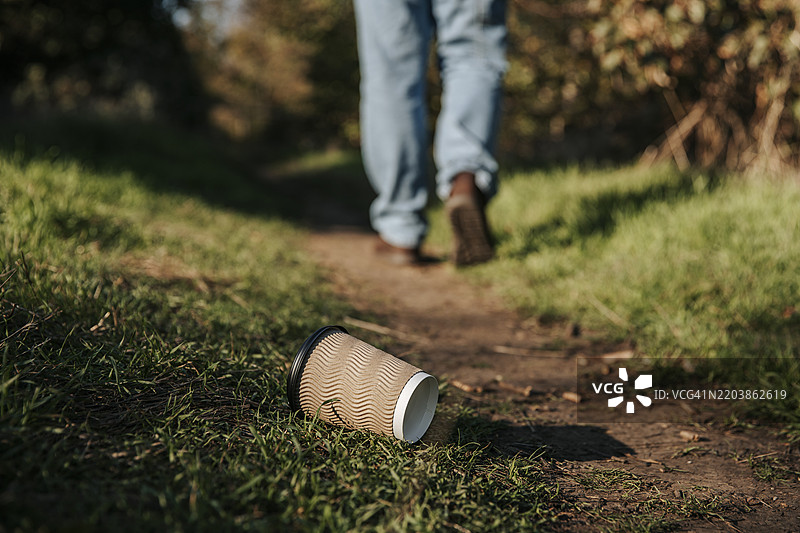 草地上放着一个咖啡杯，背景中有一个男人走过。图片素材
