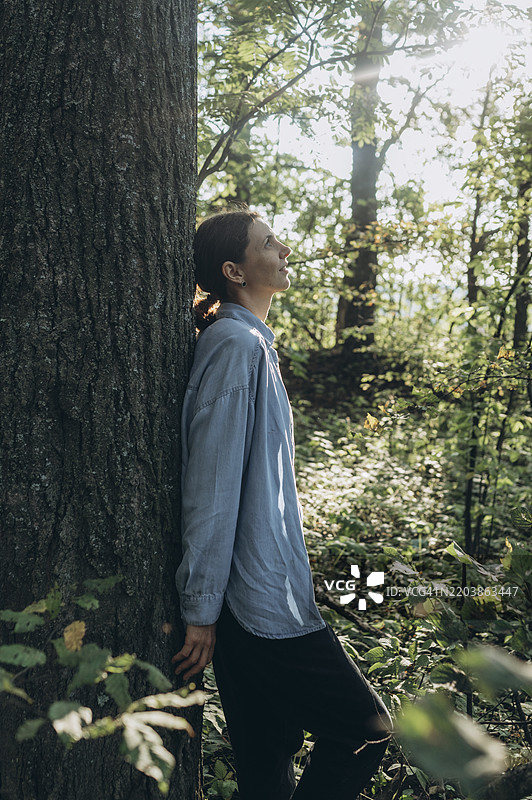 沉思的女人靠在森林中的树干上图片素材