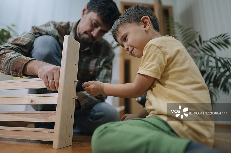 微笑的男孩在家里和父亲一起组装家具图片素材