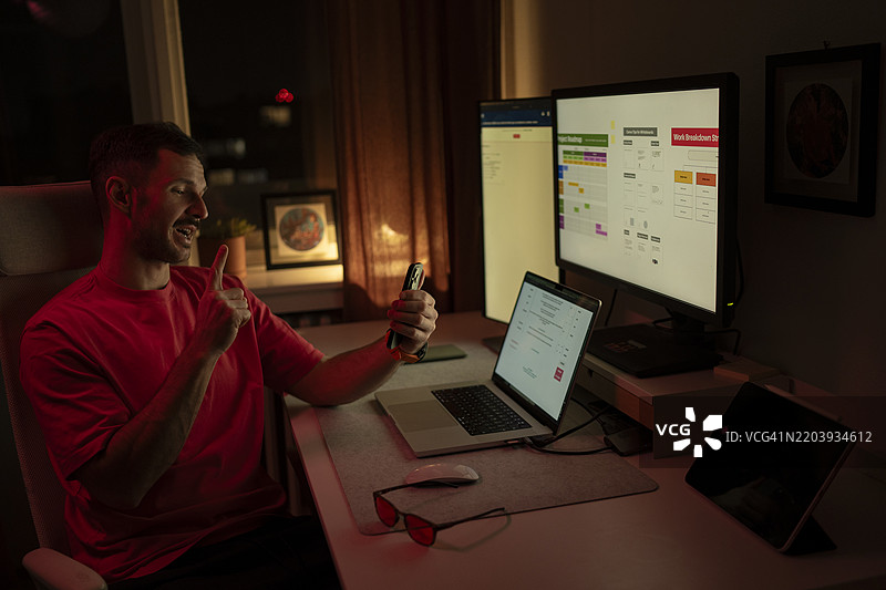 年轻男子在家工作，进行视频通话并举起手指。图片素材