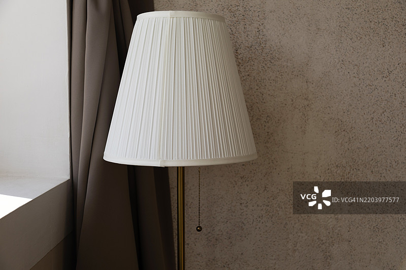 带有锥形灯罩的落地灯靠在多孔墙上。图片素材