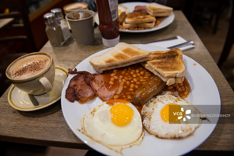 一盘英式早餐包括香肠、煎蛋、豆子、脆培根和一片烤面包。图片素材