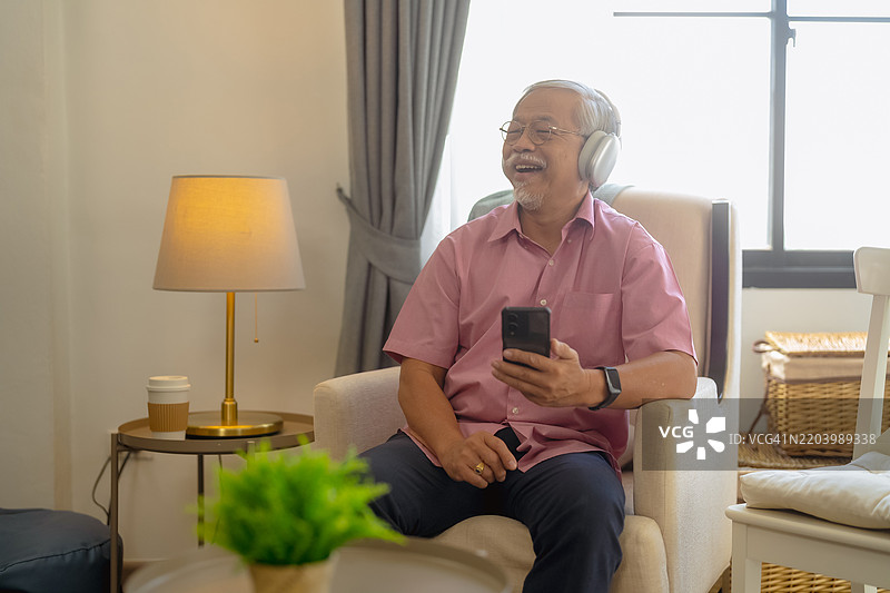 老年人放松地享受音乐与科技，戴着耳机在家中使用智能手机图片素材