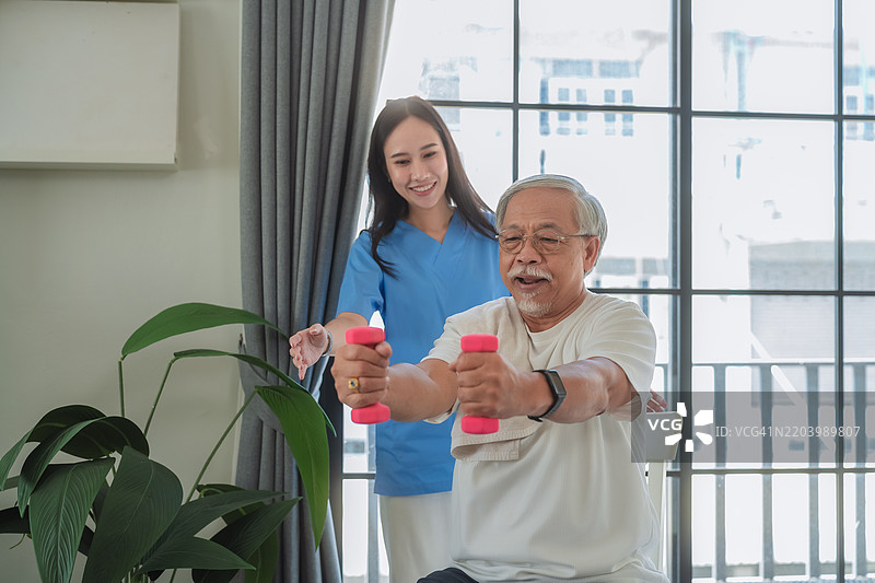 在家中进行哑铃物理治疗的患者  在家中帮助老年男性进行物理治疗的护士  医疗护理人员为老年患者进行康复拉伸图片素材