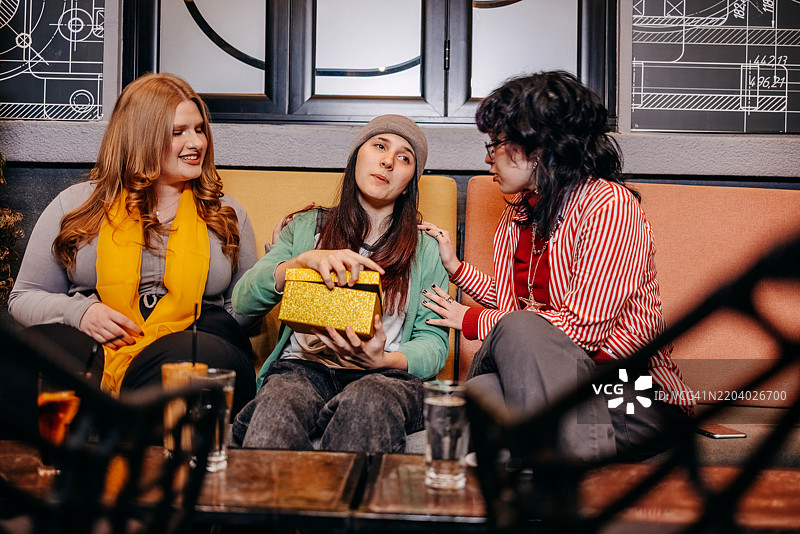 青少年女孩们在夜晚的街边咖啡馆里一起玩乐，给朋友送礼物。图片素材