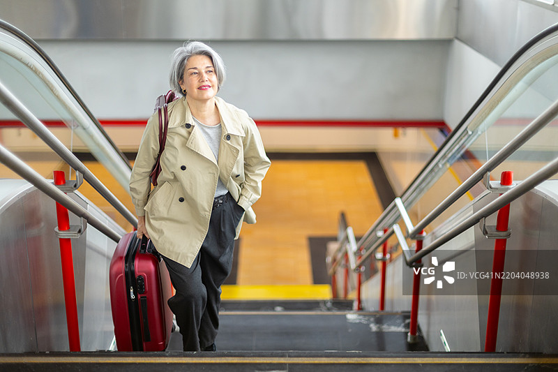 一位资深女商人提着行李箱在车站爬楼梯图片素材