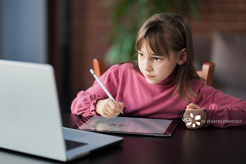 小女孩在笔记本电脑上观看在线教程，并使用数位笔和数位板绘制数字图画。图片素材
