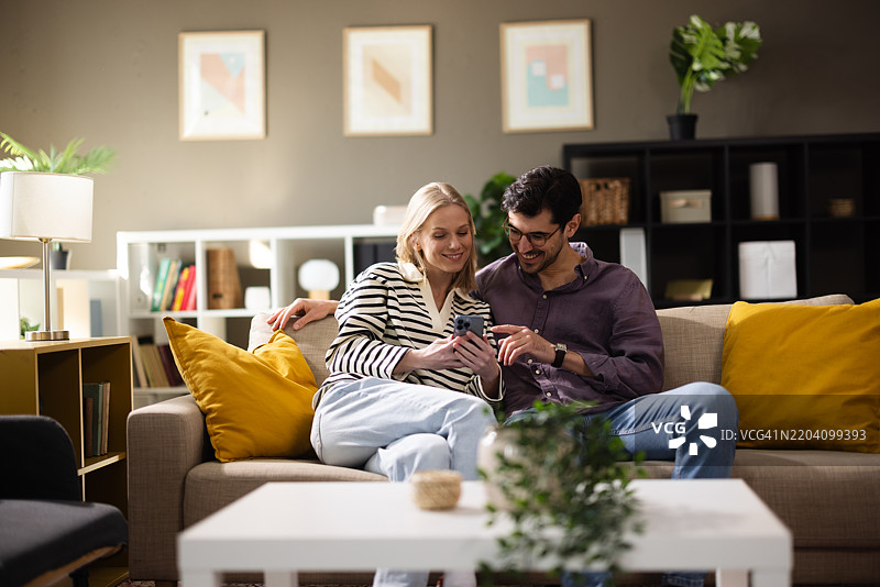 一对情侣懒洋洋地坐在沙发上，翻看他们的智能手机图片素材