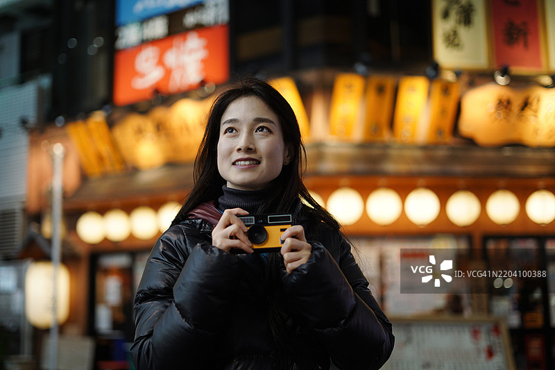 美丽的亚洲女性在东京夜晚的霓虹灯下，使用复古胶卷相机拍照，探索街道。图片素材